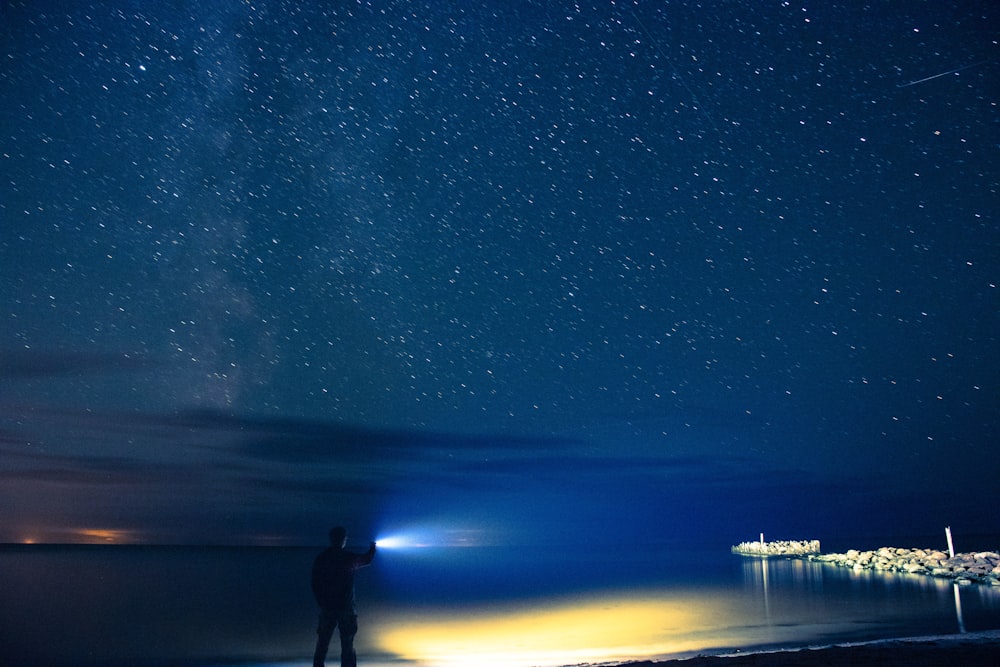 man holding flashlight standing on seashore