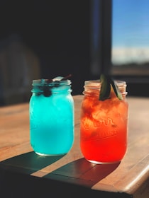 Freshly squeezed colorful fruit juices in glass jars with straws on a sunny table.