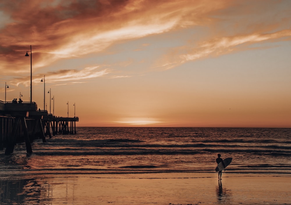 person holding surfboard walking on seashore