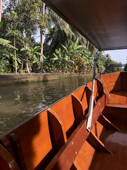 A charming illustration of knū, the canoe, gently floating on a calm river beneath a bright morning sky.