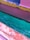 A close-up view of a boat's surface painted in vibrant colors, including pink, orange, yellow, and blue, with water seen close to the edge in a bright turquoise hue. The paint appears to be chipped and weathered with visible texture.