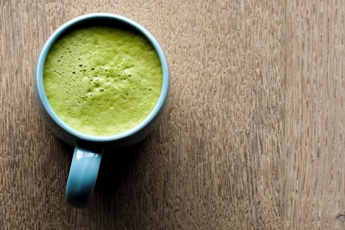 A steaming cup of frothy matcha latte on a light blue background