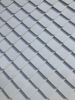 A close-up view of a pattern made up of overlapping rectangular tiles, creating a textured and uniform appearance. The tiles are arranged in a diagonal grid and are made of a smooth material.