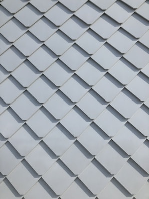 A close-up view of a pattern made up of overlapping rectangular tiles, creating a textured and uniform appearance. The tiles are arranged in a diagonal grid and are made of a smooth material.