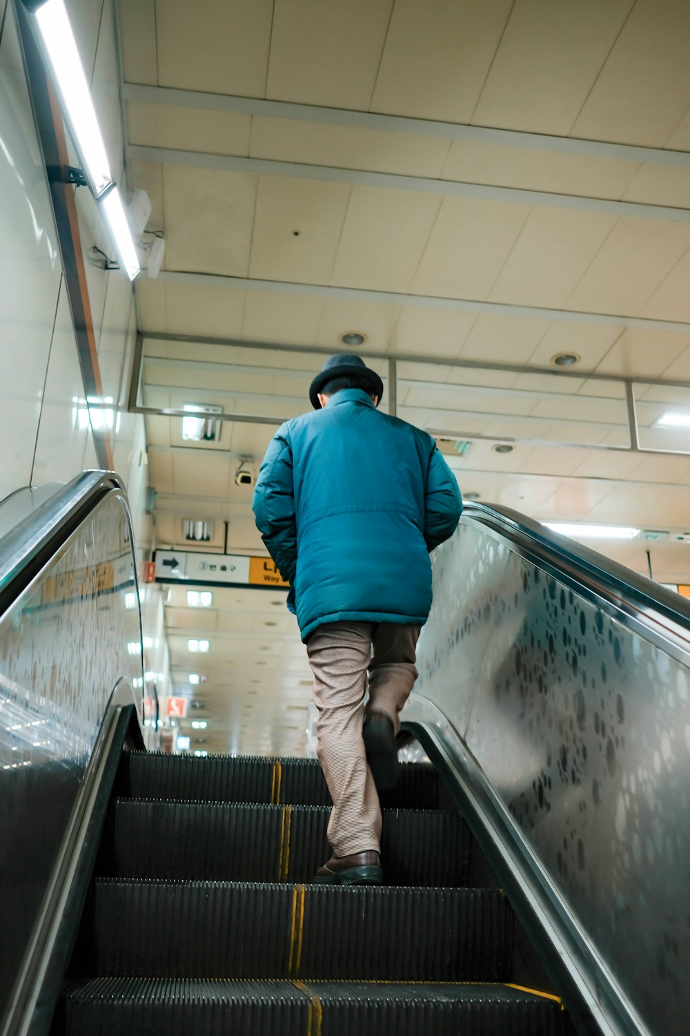 man in blue jacket going up escalator