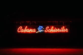 A vibrant neon sign displaying the words 'Cabana Schiorilor' with a blue skiing figure between the text. The sign is illuminated against a dark background, enhancing the glow of the red and blue lights.