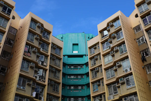 High-rise residential buildings with numerous windows and air conditioning units attached, displaying a combination of beige and teal colors under a clear blue sky.