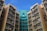 High-rise residential buildings with numerous windows and air conditioning units attached, displaying a combination of beige and teal colors under a clear blue sky.
