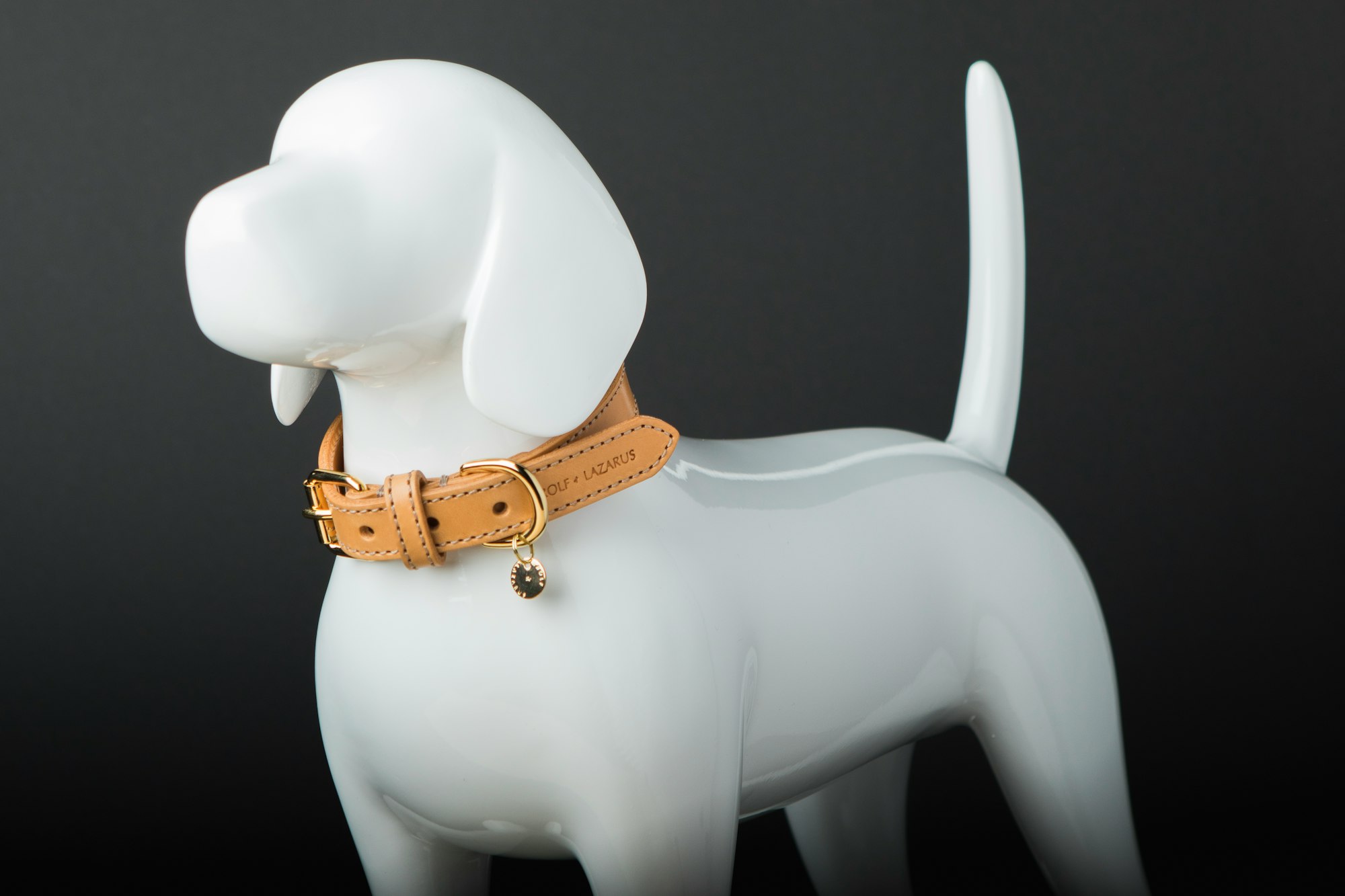 A white ceramic model of a dog with floppy ears and a straight tail, wearing a leather collar.