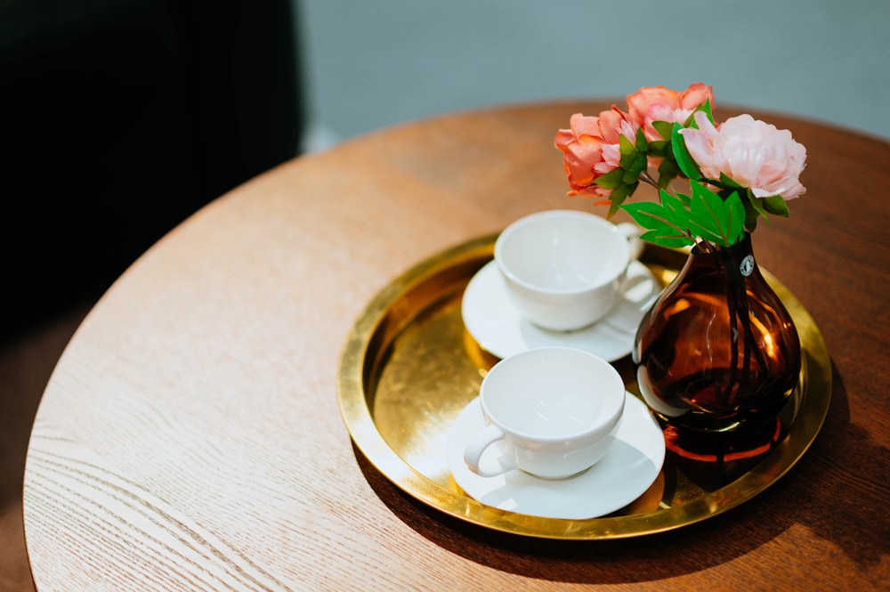 two white ceramic tea cups beside flower vase on brass-colored steel tray