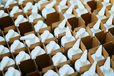 Rows of white pump dispensers are neatly packed in brown cardboard boxes, arranged closely together creating a pattern.