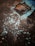 A concrete surface with peeling paint reveals patches of underlying material, with a square metallic or concrete cover embedded. The paint is chipping away, particularly around the edges of the square section, exposing a rusty color beneath the blue paint.