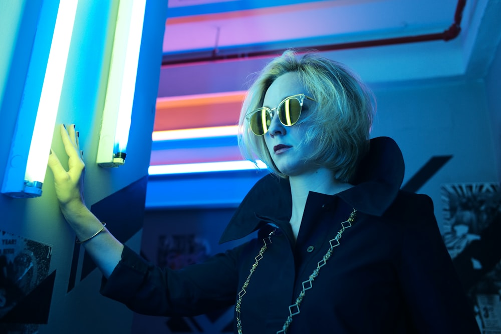 woman wearing black top and sunglasses holding on wall