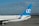 The image shows the tail section of a white aircraft with blue livery parked on an airport runway. The tail fin has a blue background with white 'oe' lettering. The side of the fuselage has a Spanish flag and the aircraft registration number 'EC-JQV'. The background consists of a cloudy sky and some distant hills.
