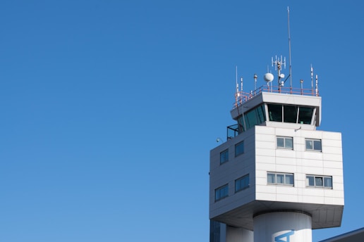 A modern air traffic control tower with a sleek design and several antennas on top set against a clear blue sky.