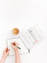 A close-up of hands writing in a notebook with a scientific textbook in the background.