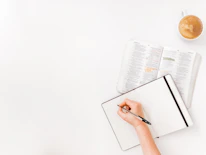 Close-up of hands writing notes for a book, surrounded by sketches and ideas.