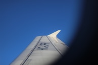 An airplane wing with visible registration markings is set against a clear blue sky. The photograph is framed in a way that features some dark, blurred edges resembling a vignette effect.