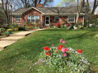 Exterior view of a charming brick house with a manicured lawn and vibrant flower beds.