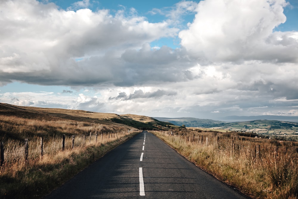 black straight road surrounded by brown field during daytime