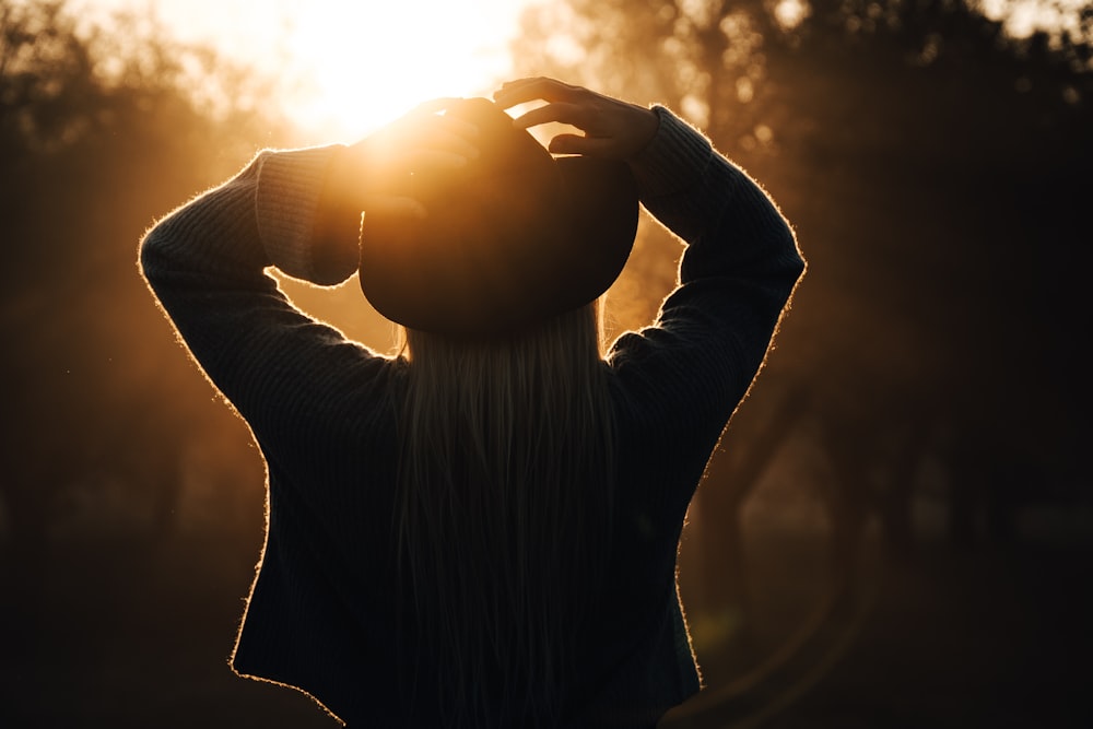 woman wearing jacket and cowboy hat while facing the trees during sunset