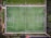 An aerial view of a rectangular soccer field with clearly marked white lines. It is surrounded by greenery and pathways, with two goals on each end of the field. The field appears to be well-maintained with vibrant green grass.