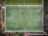 An aerial view of a rectangular soccer field with clearly marked white lines. It is surrounded by greenery and pathways, with two goals on each end of the field. The field appears to be well-maintained with vibrant green grass.