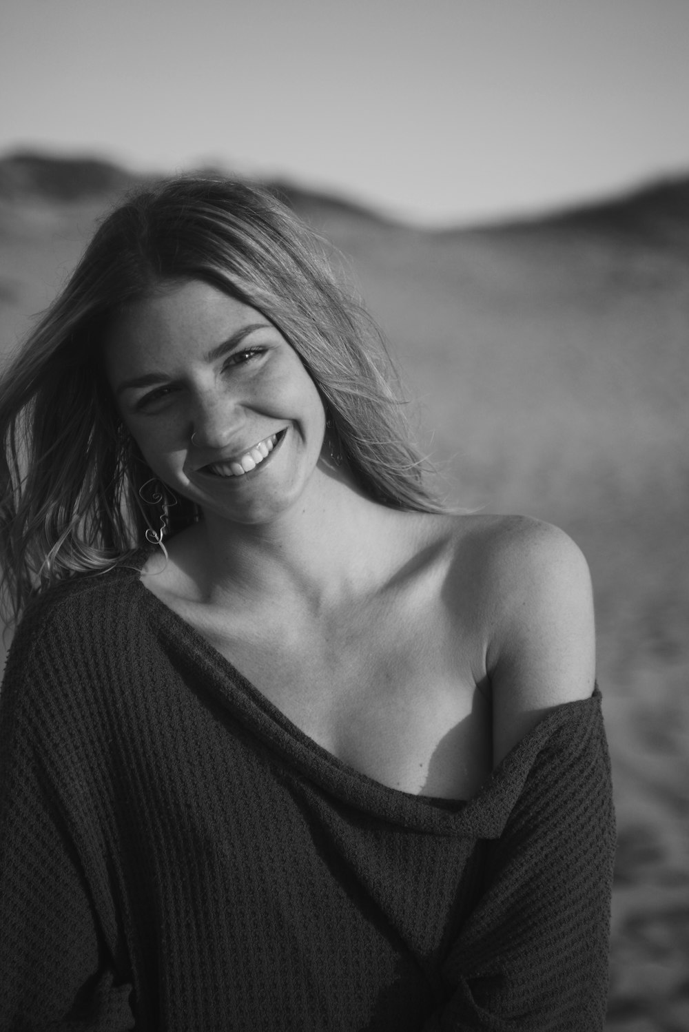 greyscale photo of woman wearing off-shoulder shirt while smiling