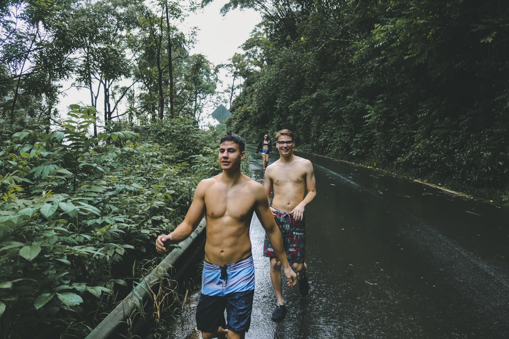 two topless man walking on wet road during daytime