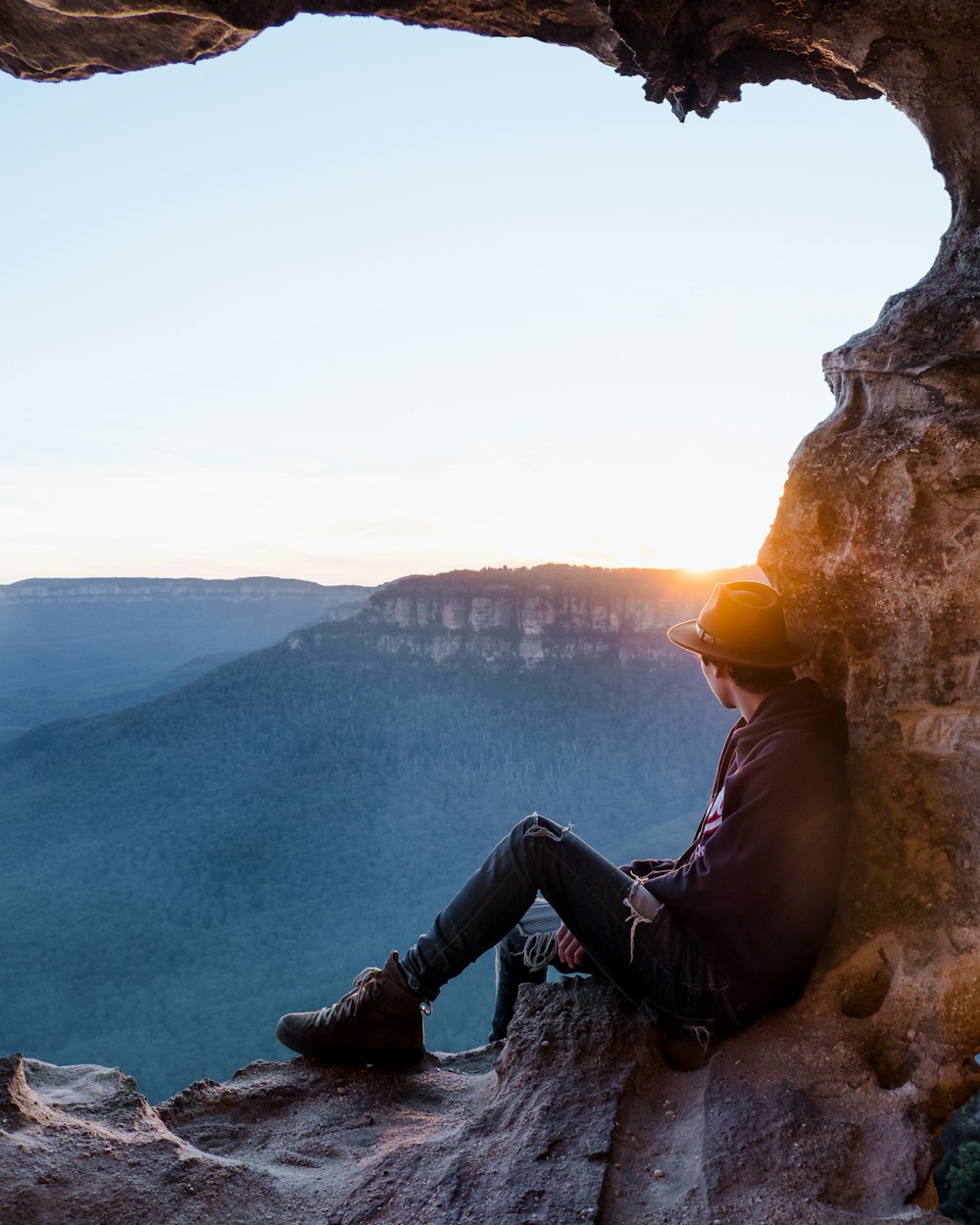 man sitting on cliff during sunset