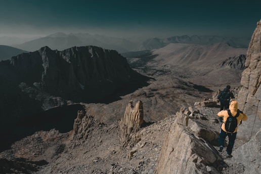 Hikers walking along a forested mountain path with panoramic views of rugged peaks.