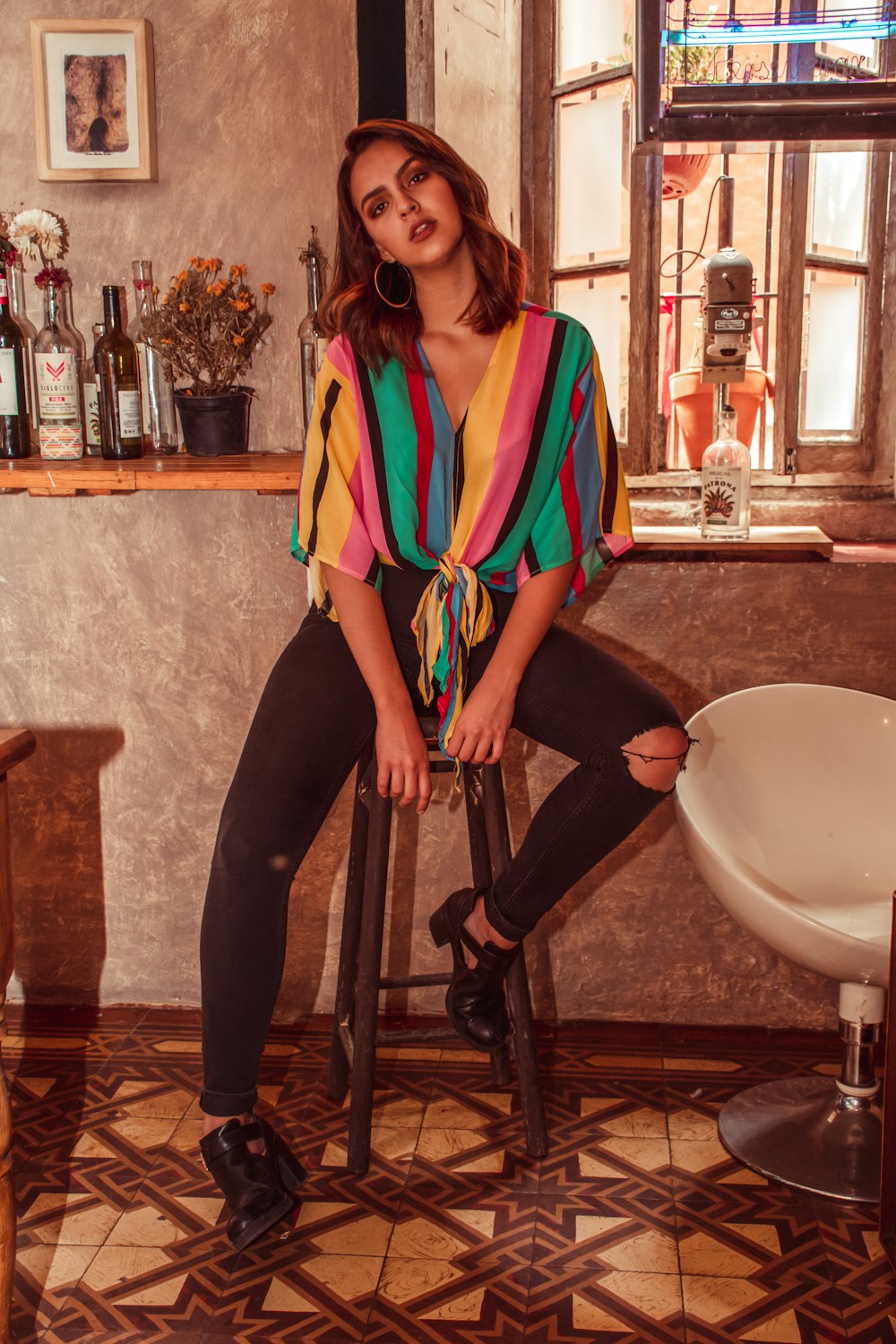 woman in yellow, pink, green, and red vertical striped top sitting on bar stool