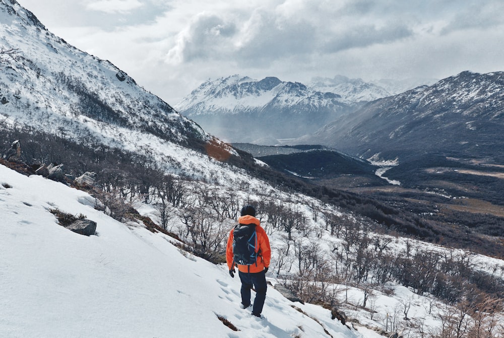 person wearing orange jacket with black pants walking on snow covered field during daytime