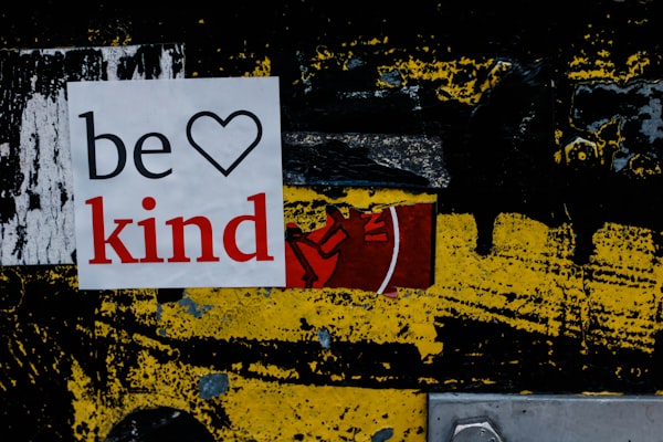 A billboard poster on a wall displaying the text 'be kind' with a heart logo