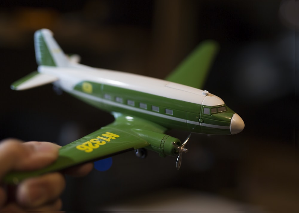 person holding white and green plastic airplane toy