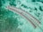 Aerial view of a series of overwater bungalows forming a curved line in a turquoise lagoon, showcasing clear waters with patches of darker green coral beneath.