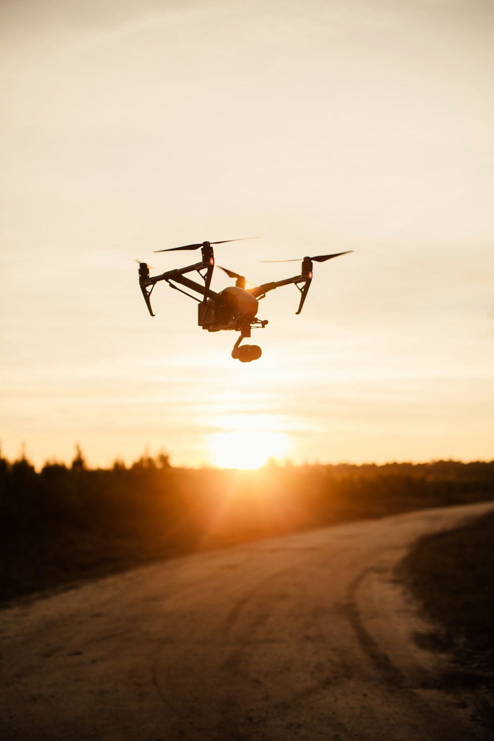 silhouette of black quadcopter above road during golden hour