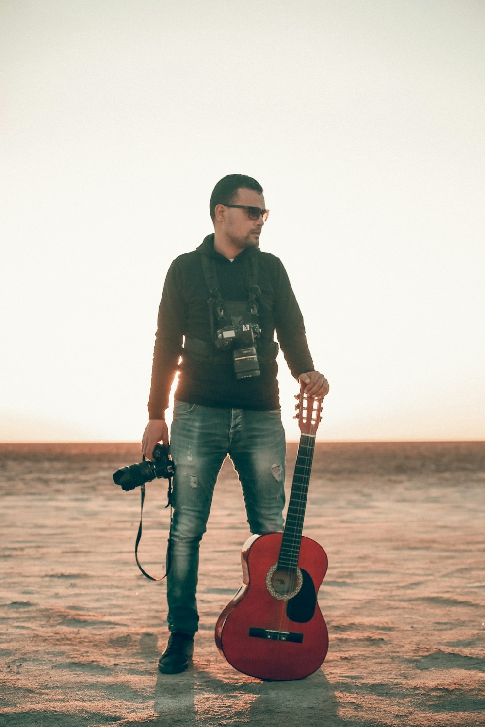 man holding classical guitar with left hand and DSLR camera on right hand