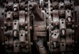 Complex machinery parts with heavy rust and wear, featuring interlocking gears and metal components. The image captures intricate details of industrial equipment showcasing bolts, nuts, and mechanical textures.
