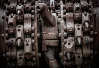 Complex machinery parts with heavy rust and wear, featuring interlocking gears and metal components. The image captures intricate details of industrial equipment showcasing bolts, nuts, and mechanical textures.