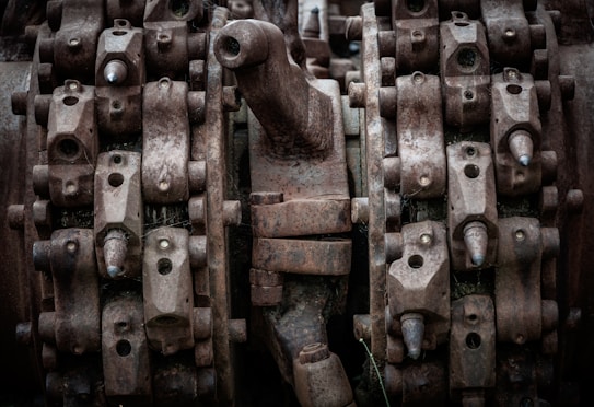 Complex machinery parts with heavy rust and wear, featuring interlocking gears and metal components. The image captures intricate details of industrial equipment showcasing bolts, nuts, and mechanical textures.