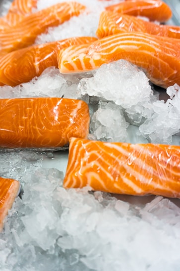 Close-up of freshly caught salmon fillets glistening on crushed ice with a soft blue background.