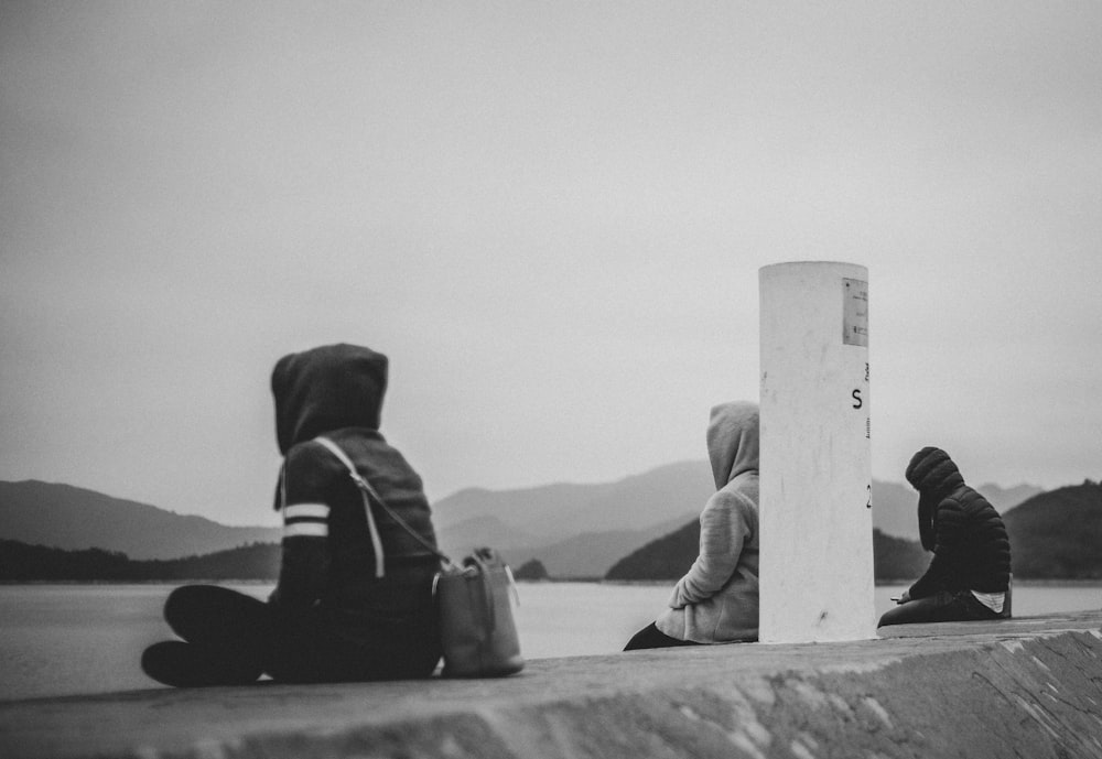 three person sitting near body of water