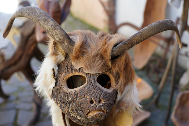 A rust-stained mask featuring twisted, asymmetrical horns and textured layers of torn paper.