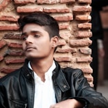 A candid shot of a man leaning against a textured brick wall, eyes closed in thought.