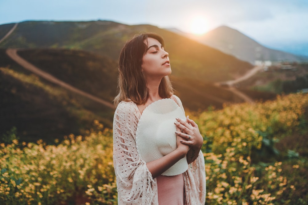 woman holding white hat while standing on yellow flower field