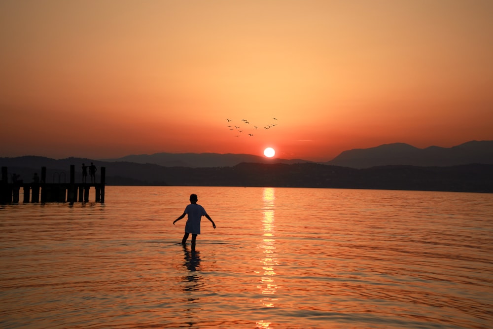 man walking in sea under golden hour
