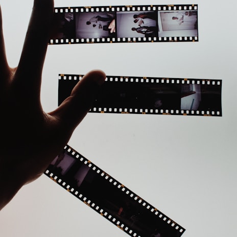 Hands gently holding a freshly developed strip of 120 film negatives in a dimly lit darkroom.