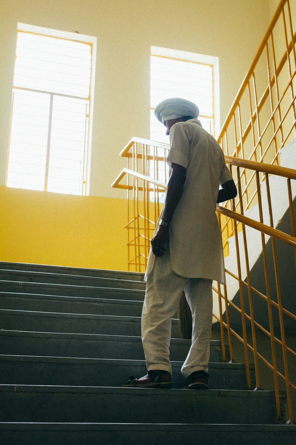 Mann in schwarzer Jacke und grauer Hose steht auf gelber Treppe
