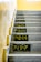 A staircase with multiplication tables painted on each step in bold yellow numbers against a black background. The walls are a light beige, and the steps are concrete.